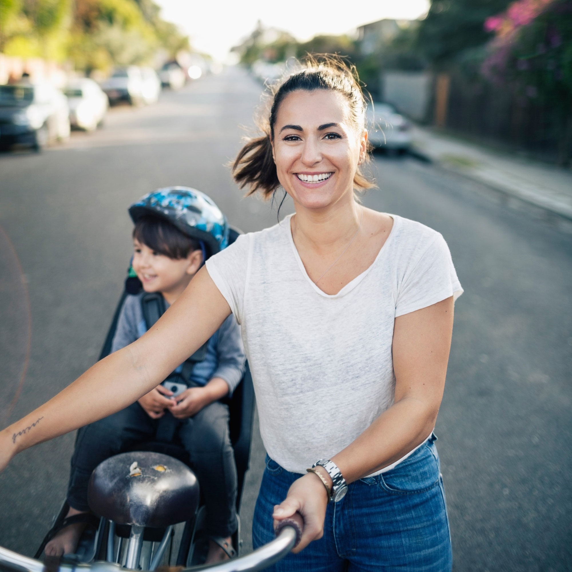 Glad kvinna går på en väg och leder en cykel. på pakethållaren sitter ett glatt barn i en cykelstol